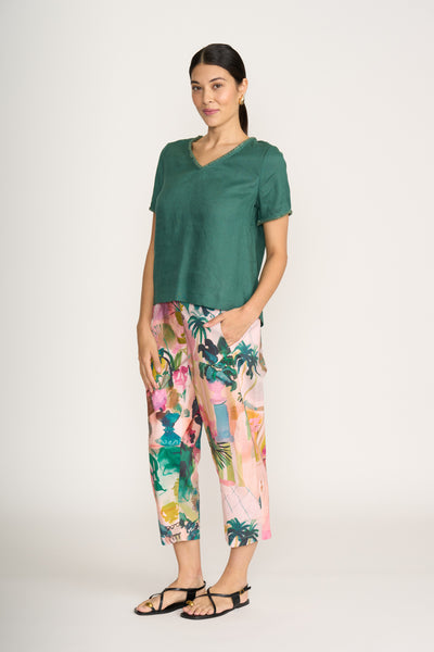 Woman wearing a green top and colorful tropical print pants on a white background