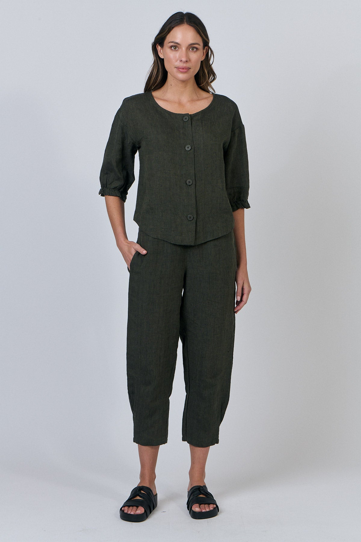 Woman wearing a dark green outfit with a buttoned top and cropped pants on a white background