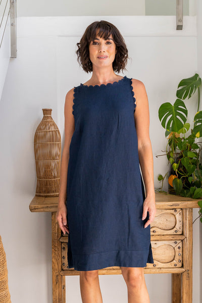 Woman wearing a navy dress standing in a room with a wooden shelf and plants.