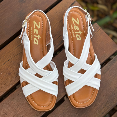 White sandals with brown soles on a wooden surface, featuring the brand 'Zeta'.