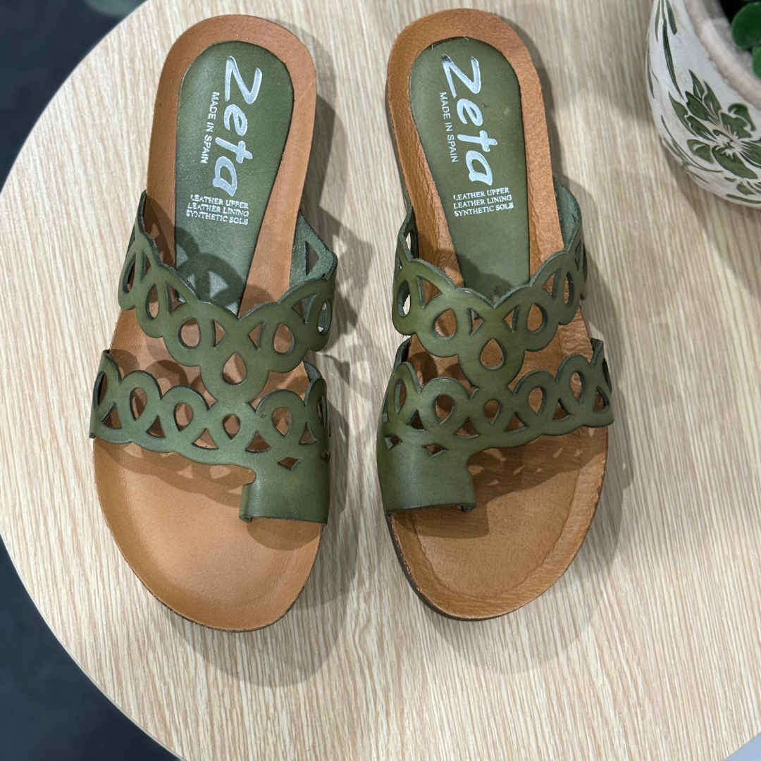 Green sandals with cut-out design on a light wooden surface, brand 'Zeta' visible.
