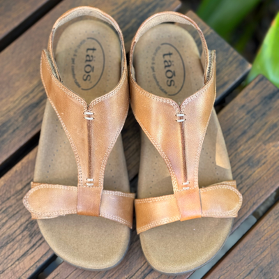 Pair of tan sandals with 'taos' branding on a wooden surface