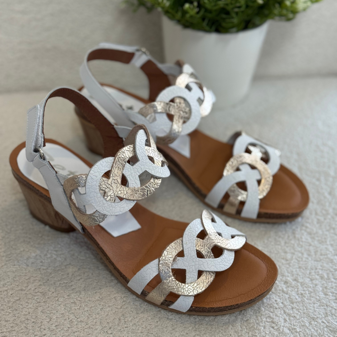 Pair of sandals with gold and white  straps on a light surface.