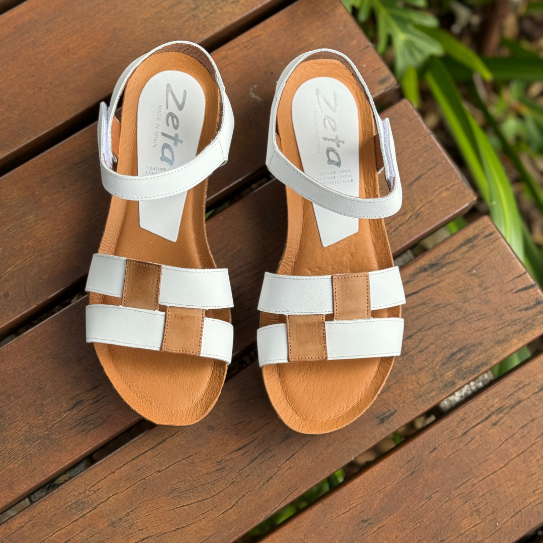 Pair of tan and white sandals on a wooden surface with 'Zeta' branding.