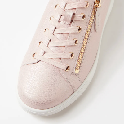 Pink sneaker with gold laces and zipper on a light background