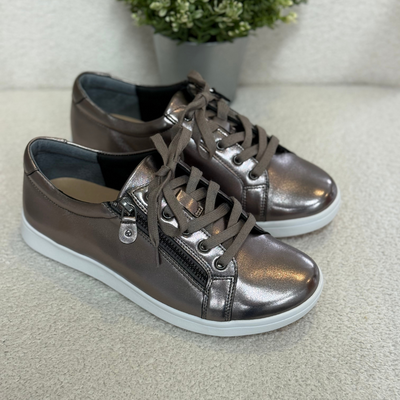 Pair of metallic pewter sneakers on a light surface with a plant in the background