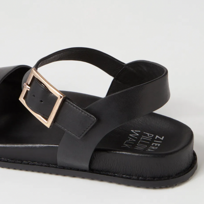 Black sandal with a gold buckle on a light gray background